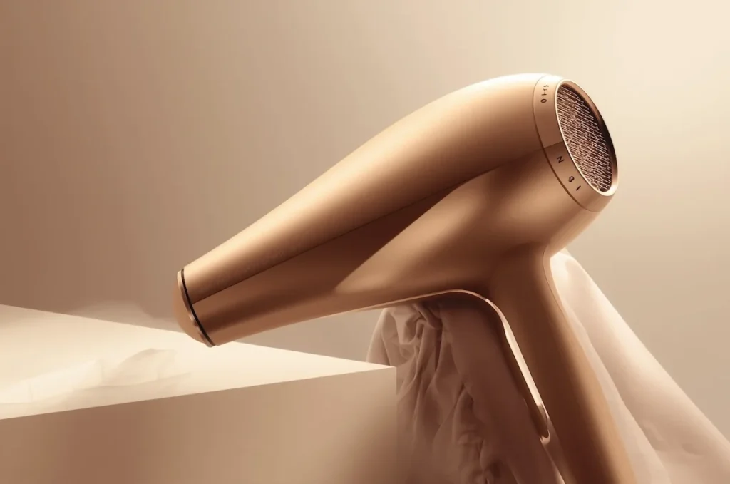 Primo piano di un asciugacapelli dorato con design elegante e moderno, fotografato su sfondo beige minimalista.